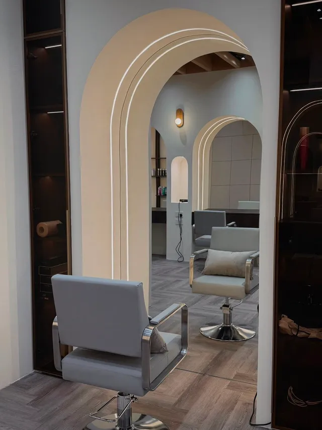 Looking through a lit archway from one chair to the next station, where a cushion waits on the seat.
