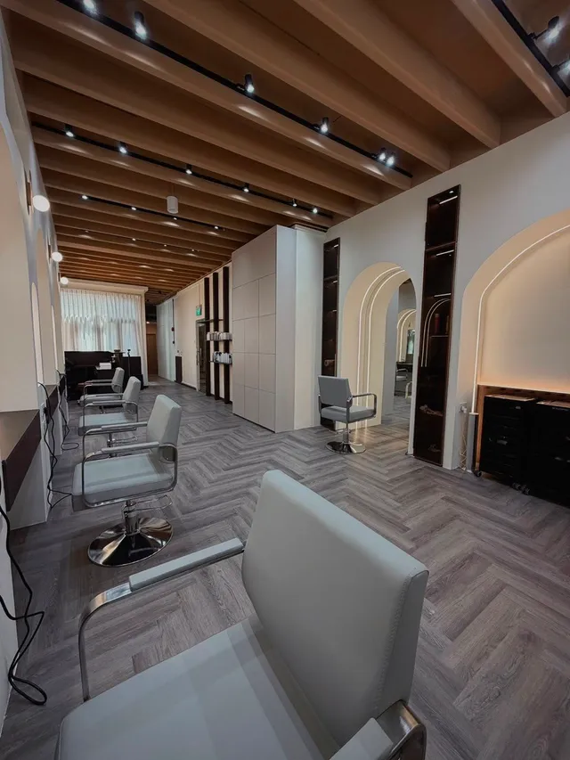Pale grey styling chairs on a herringbone floor beneath timber beams, each station set into a softly lit arch.