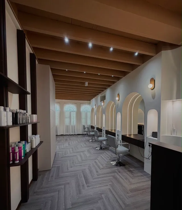 The length of the studio on Pagoda Street: product shelves on one side, arched mirrors and warm sconces on the other, and three shuttered shophouse windows at the far end.