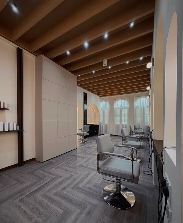 Daylight through sheer curtains at the front windows, falling across a row of chairs and the herringbone floor.